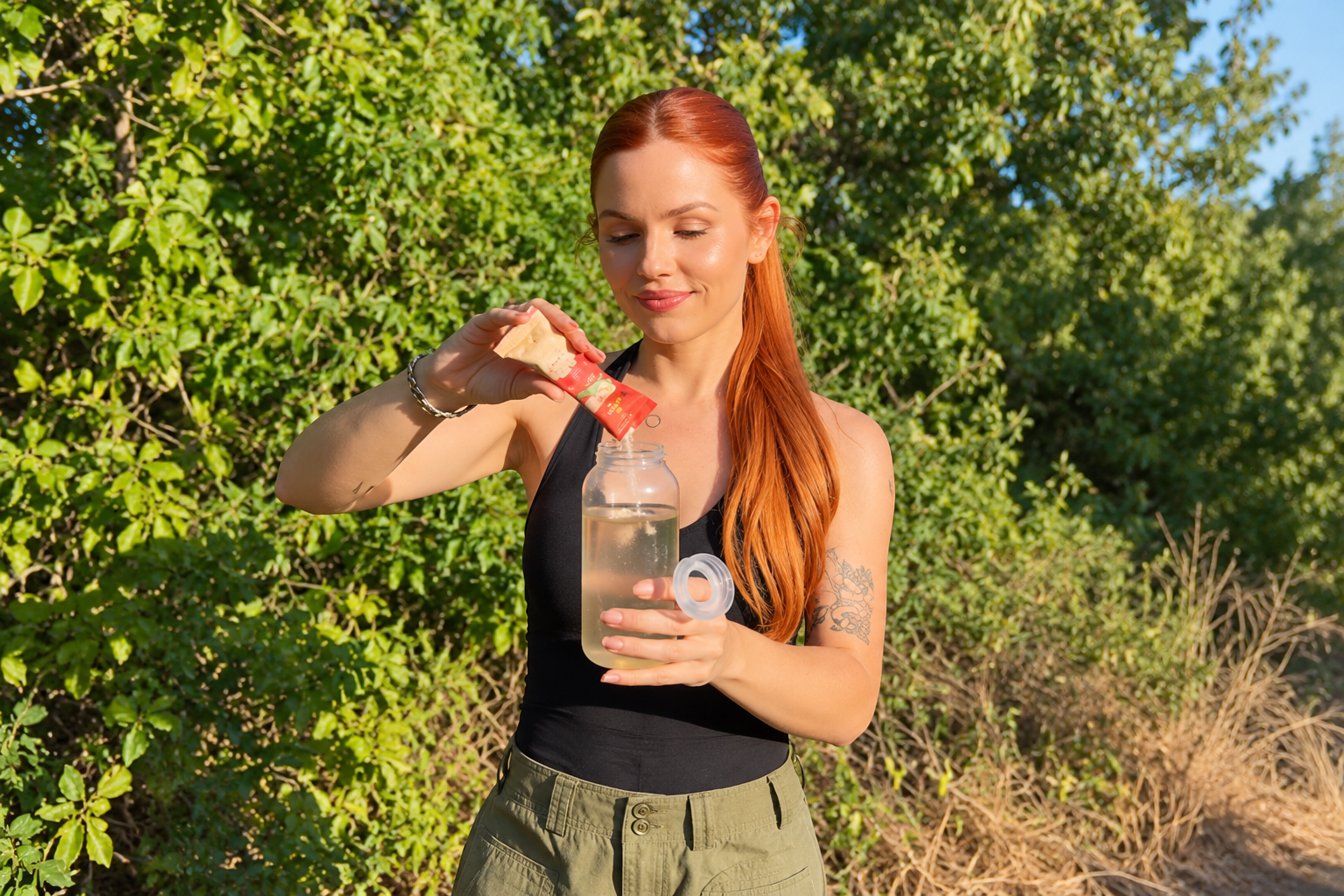A woman pours a Tuyyo Foods Agua Fresca sachet into a water bottle outdoors.