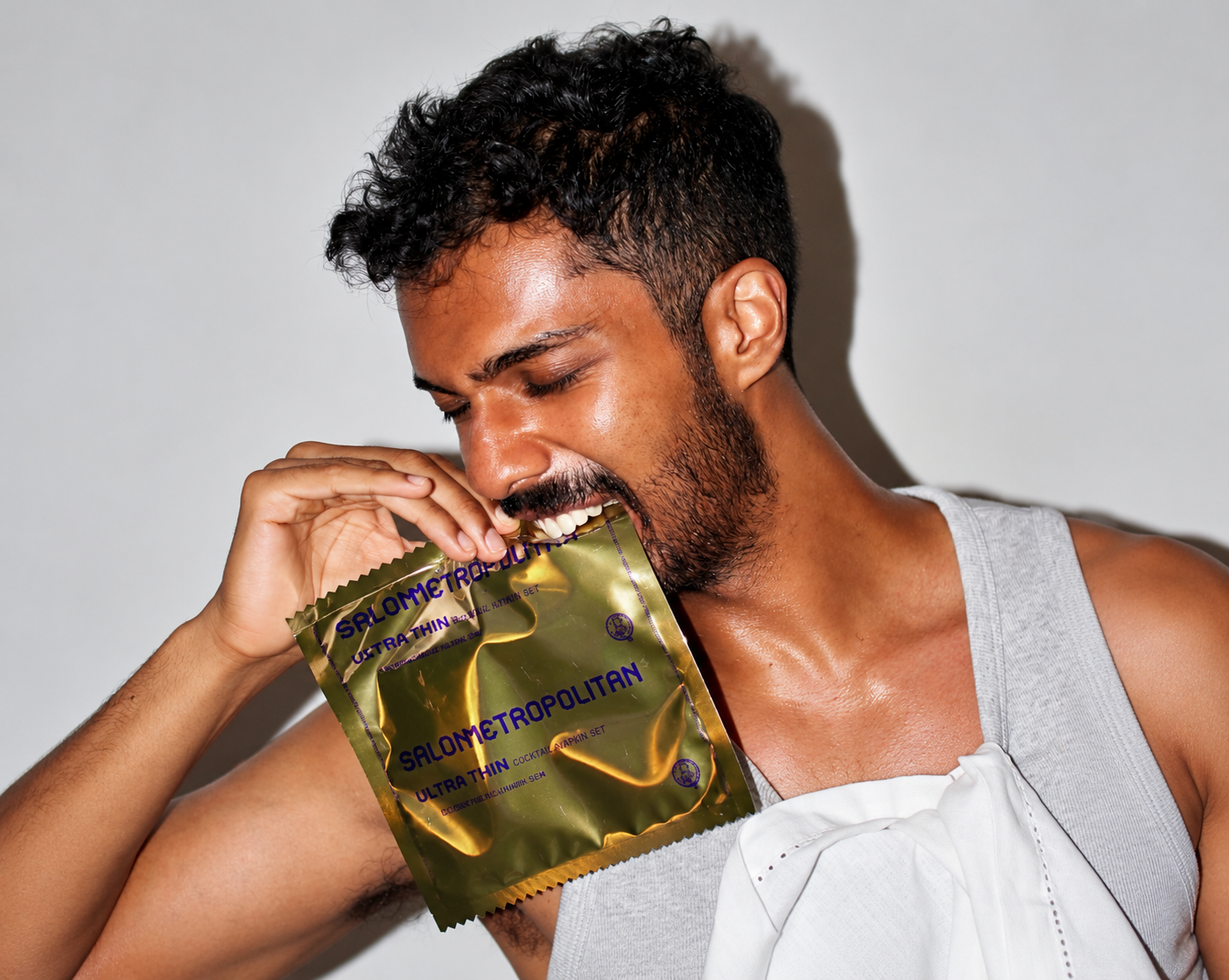 A man holds a reflective gold Salon Metropolitan sachet near his face while holding a white cocktail napkin.