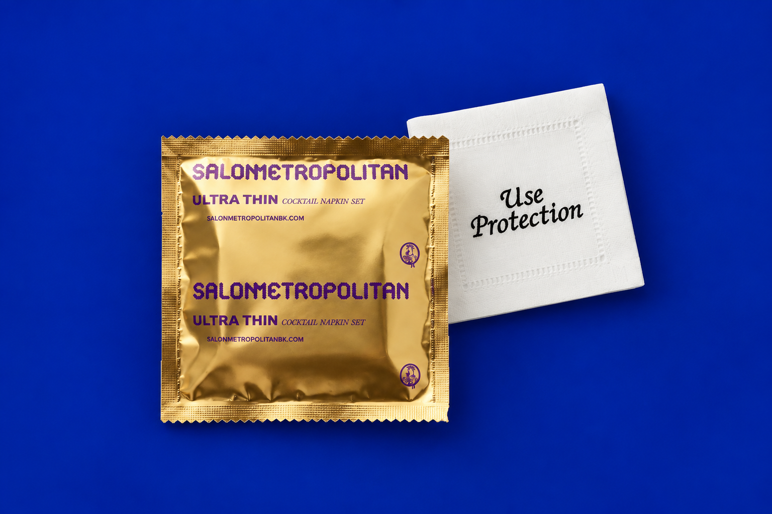 A gold Salon Metropolitan Ultra Thin cocktail napkin sachet and a white napkin are displayed on a blue background.