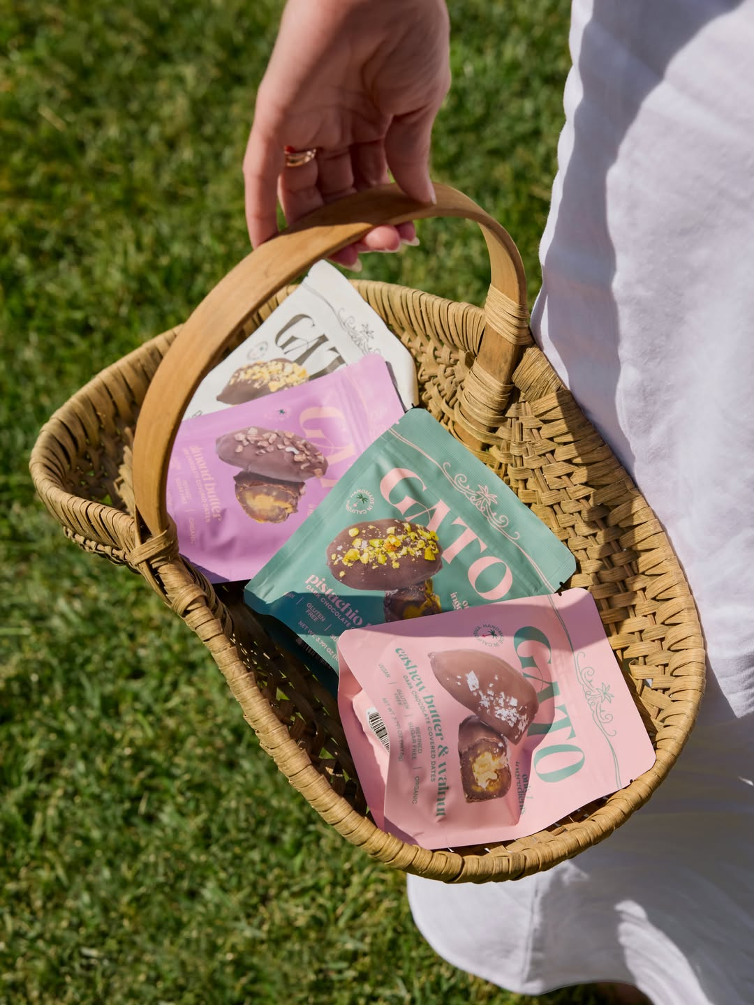 Gato pouches in pink, green, purple, and cream carried in a woven basket outdoors.