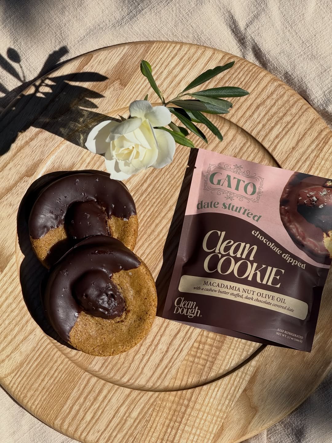 Gato and Clean Dough date-stuffed cookie pouch beside chocolate-dipped cookies and a white rose on a wooden board.