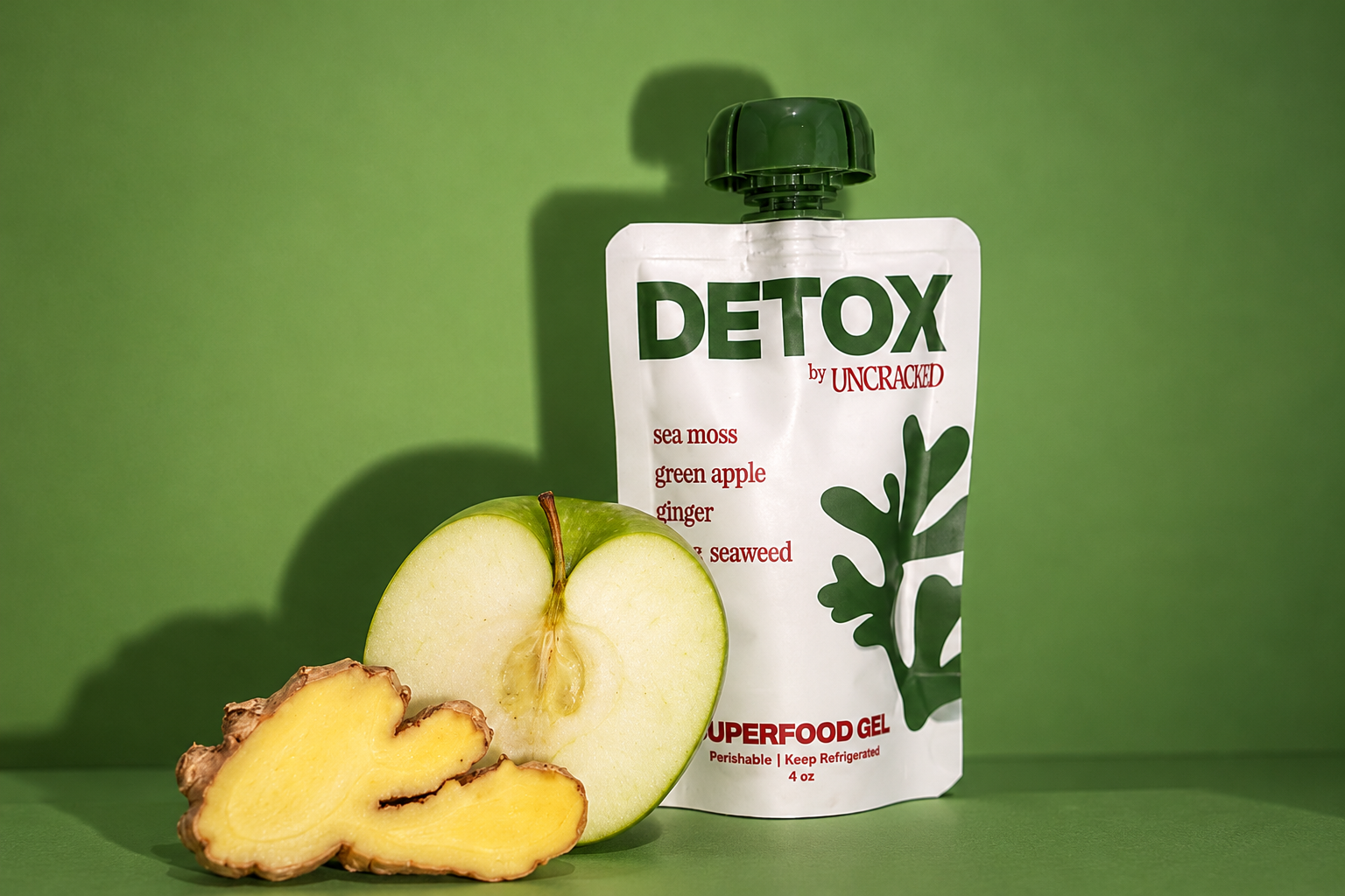 An Uncracked Detox spouted pouch stands with green apple and ginger against a green background.