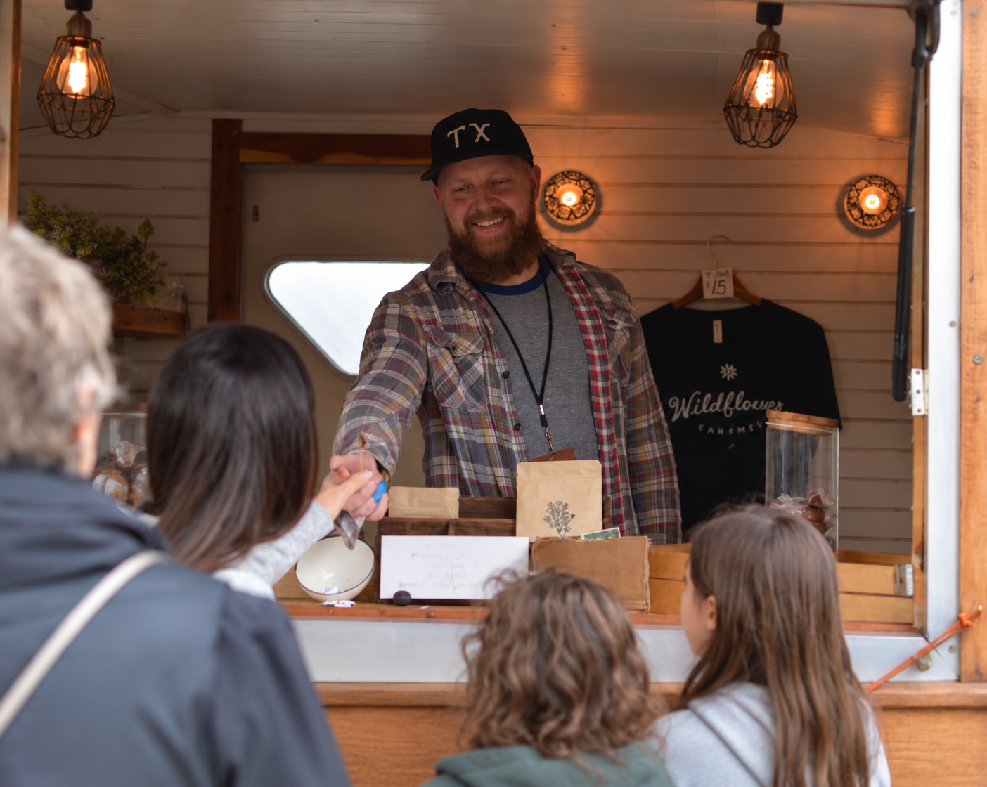 A Wildflower Caramel Co. vendor hands a sample to customers at a market stall.