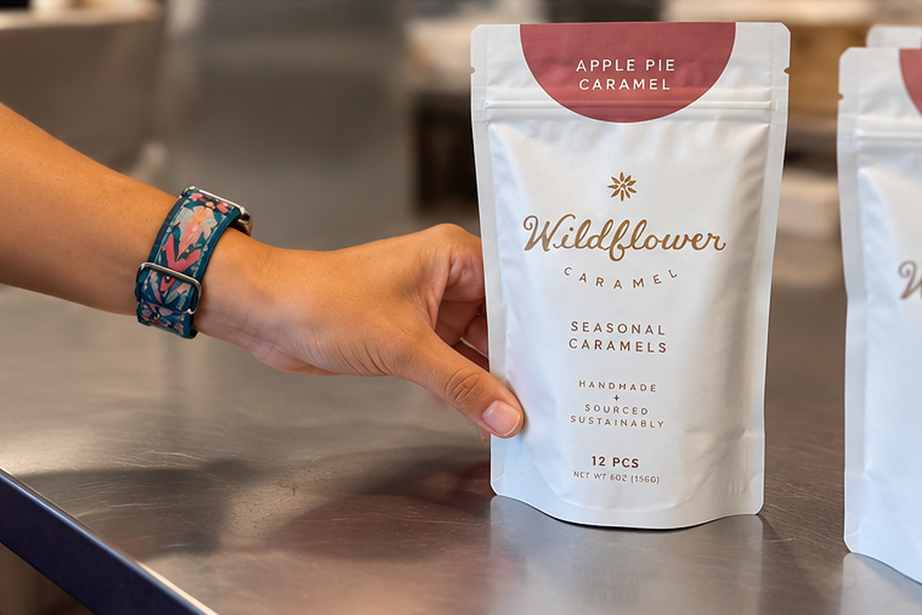 A hand displays a finished white Wildflower seasonal caramel pouch on a workbench.