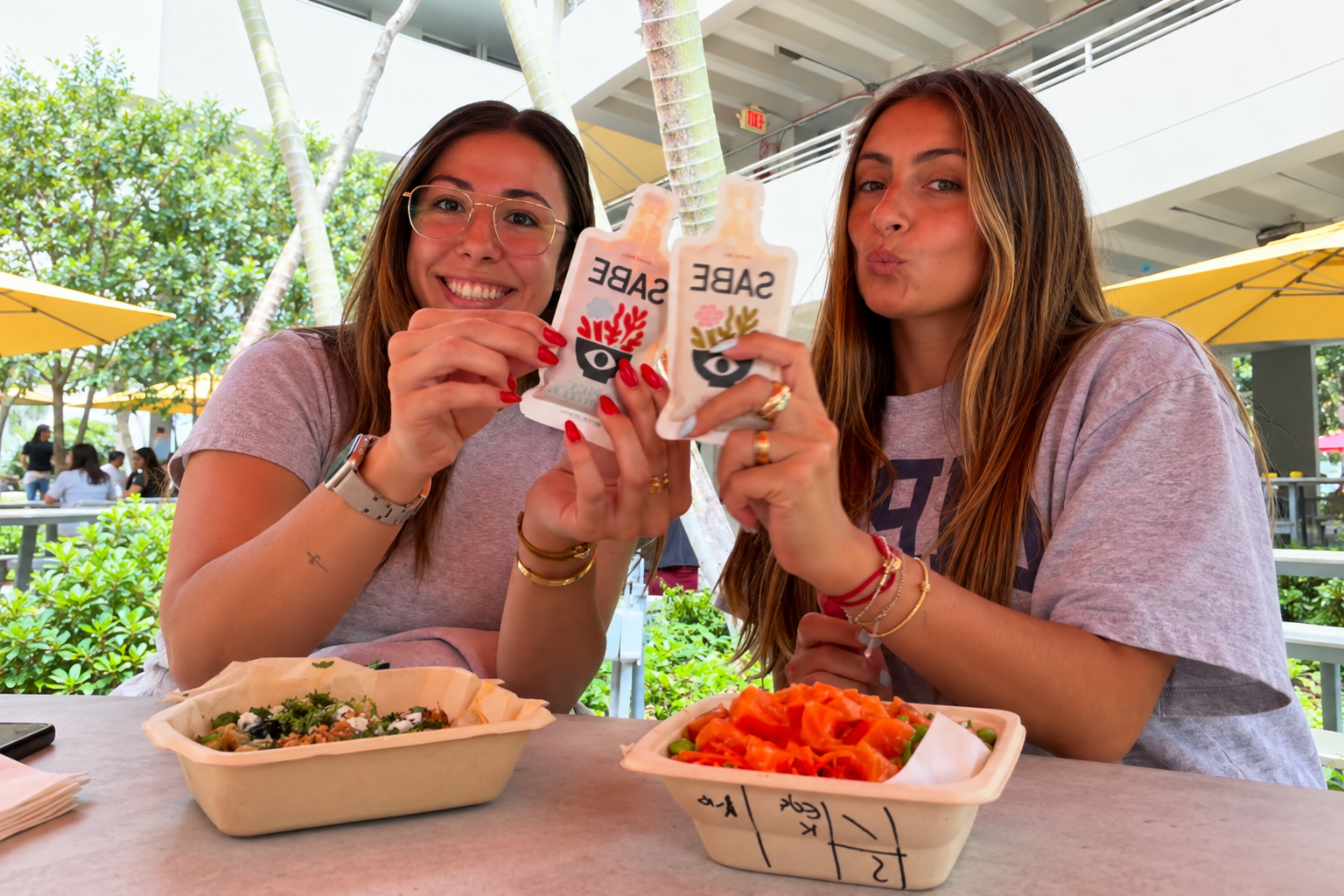 Two people holding SABE sauce pouches over prepared meals