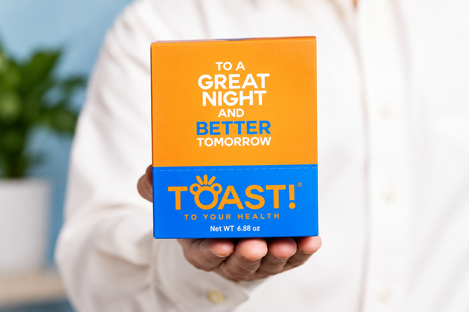 A person holds an orange and blue Toast! retail carton upright with its front panel facing the camera.