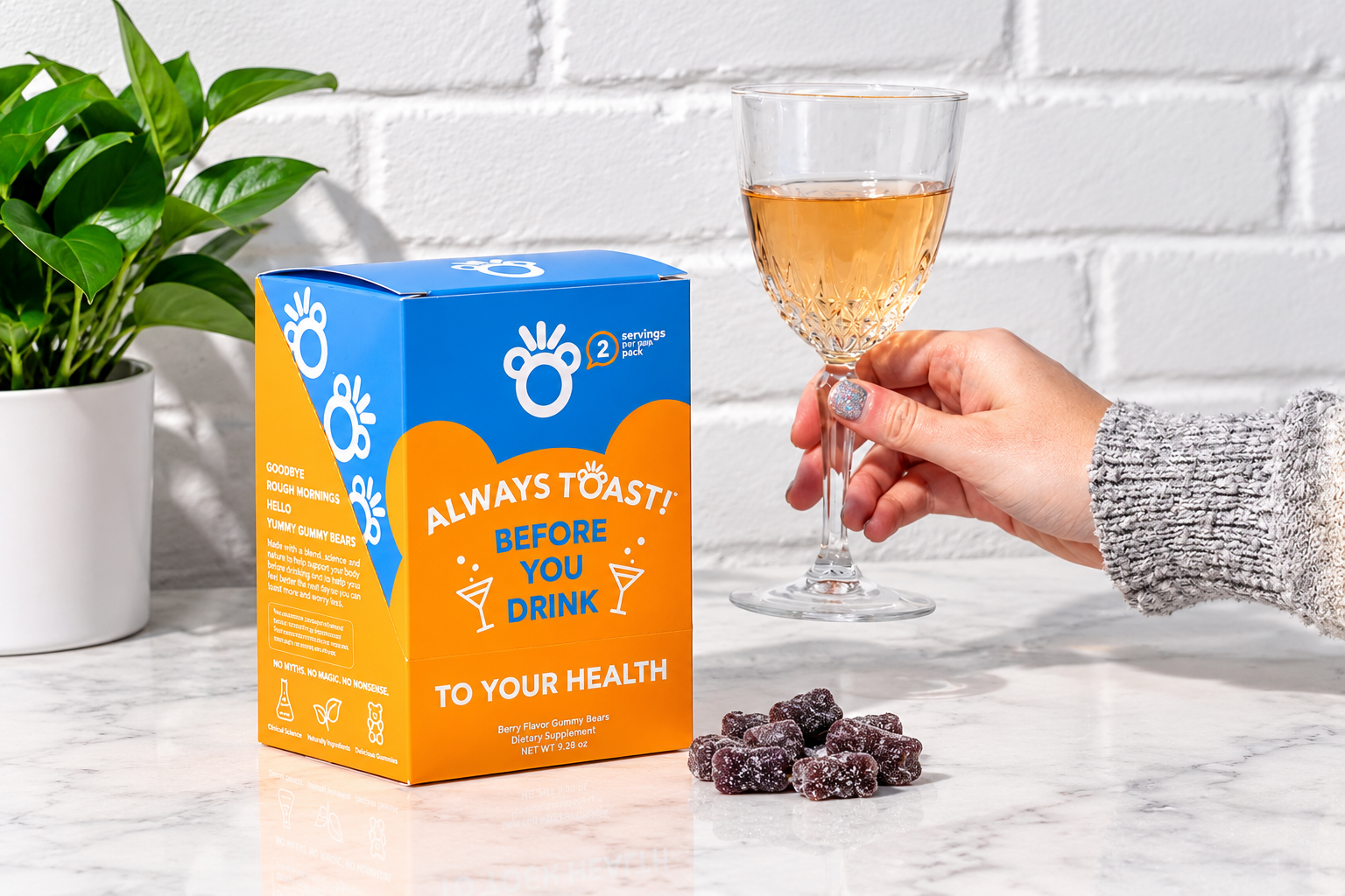A Toast! retail carton and dark gummies sit on a marble surface while a hand holds a glass of amber-colored drink.