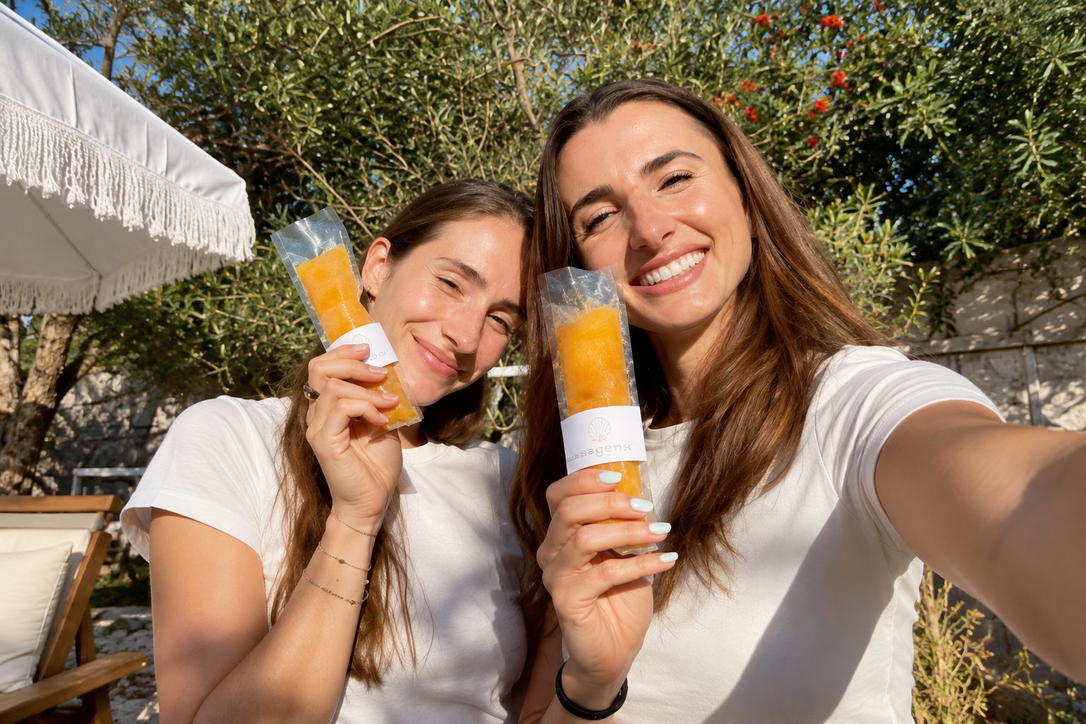 Klaudia and Kat smile outdoors while holding orange Sea Gems popsicles.