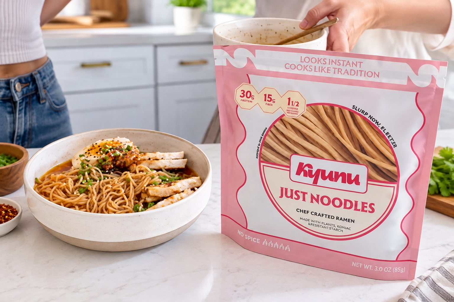 A pink KYUNU Just Noodles pouch stands beside a prepared noodle bowl in a kitchen.