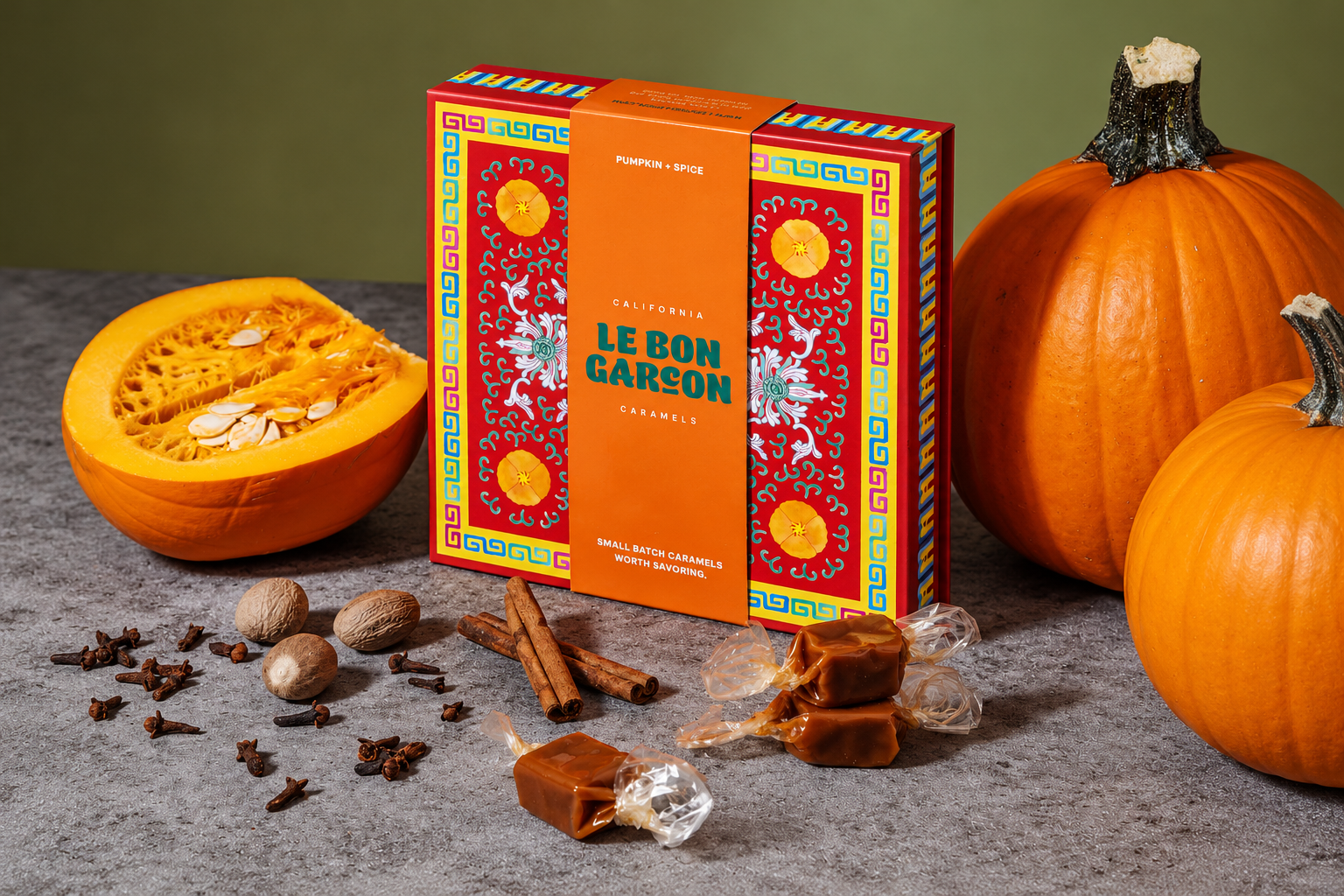 A colorful Le Bon Garçon caramel box is displayed with pumpkins, citrus, spices, and wrapped caramels.