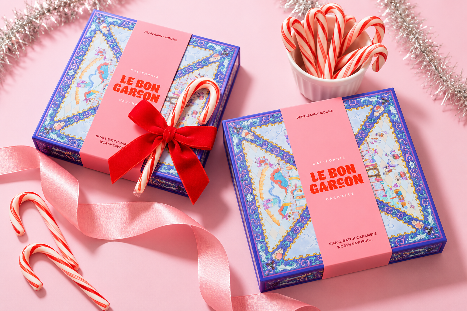 Blue and pink Le Bon Garçon rigid boxes are arranged with red ribbon and candy canes.