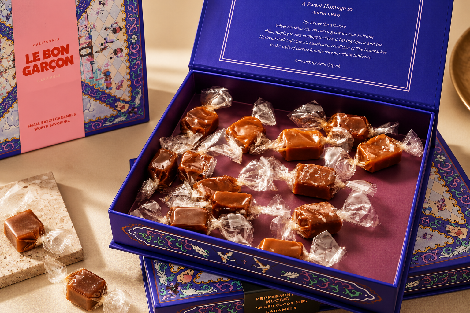 An open blue Le Bon Garçon rigid box holds individually wrapped caramels beside matching boxes.